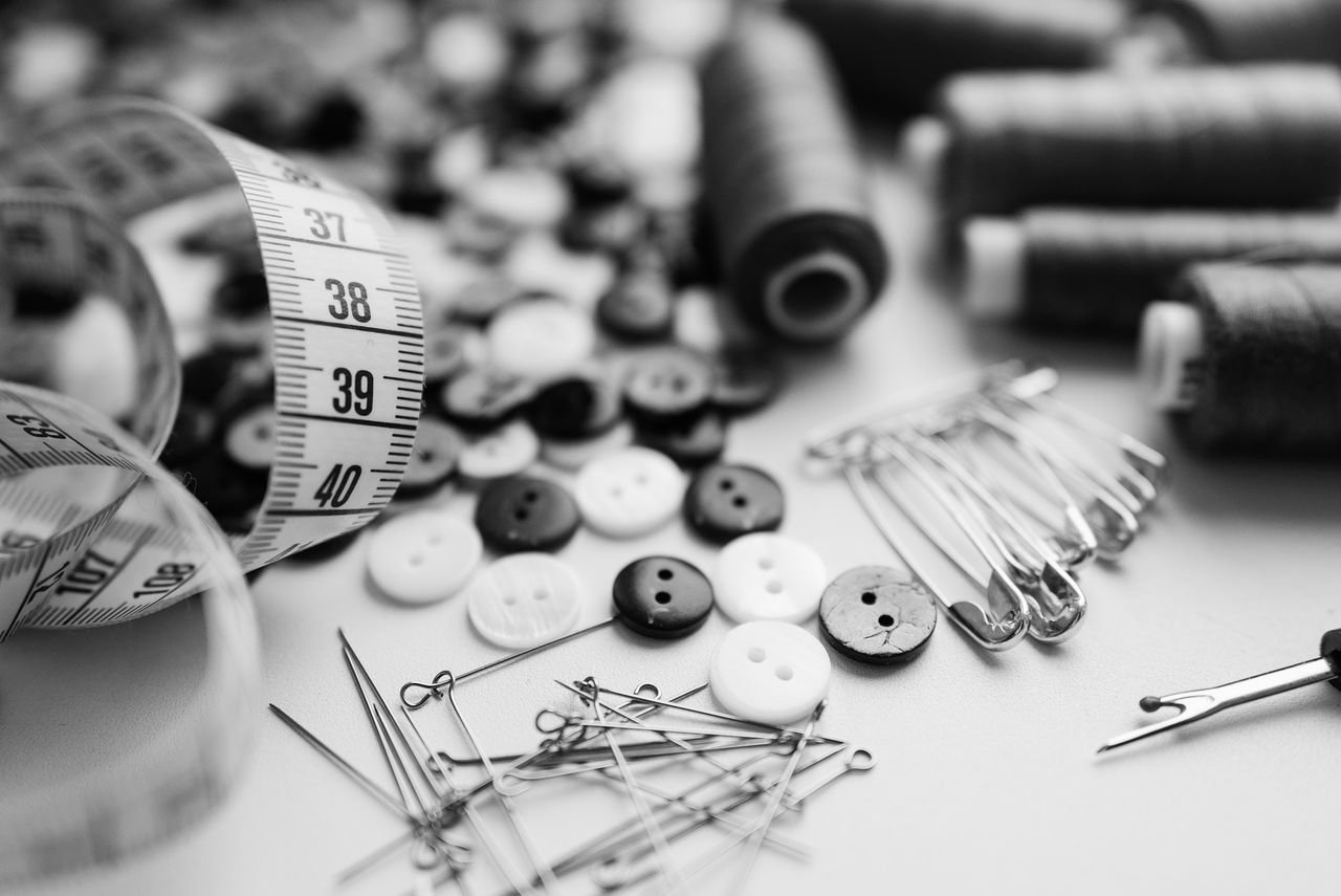gallery-5 Black and white sewing materials including buttons, needles, and thread spools on a white surface.