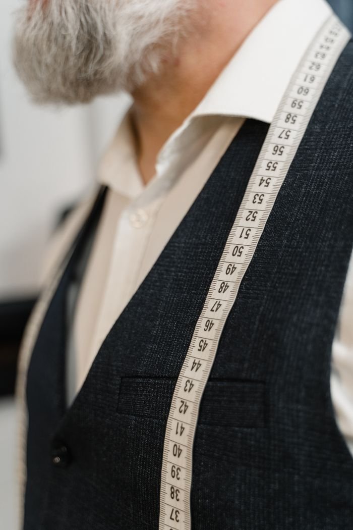 why-choose-us Close-up of a tailor in a suit with a measuring tape across his shoulders.